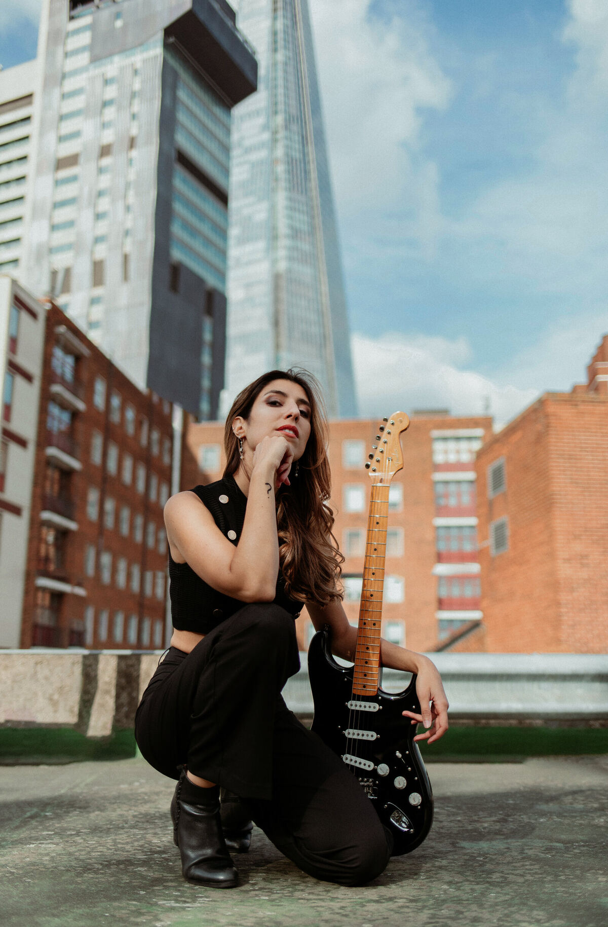 Alba crouched with her guitar on a London rooftop, the Shard visible behind her